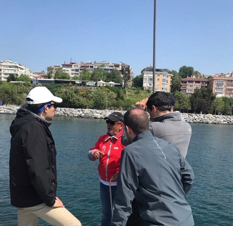 Yelken kursunda eğitmen, teknede öğrencilere manevra ve yelken kontrolü anlatırken